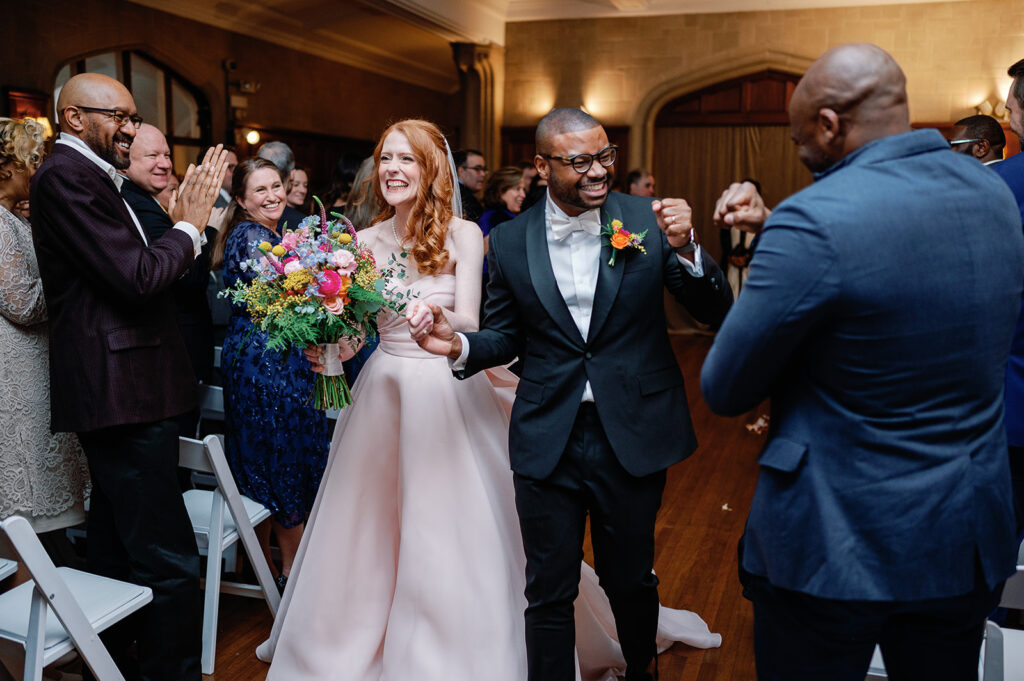 Bride wearing pink dress with colorful bouquet and groom walking down the aisle