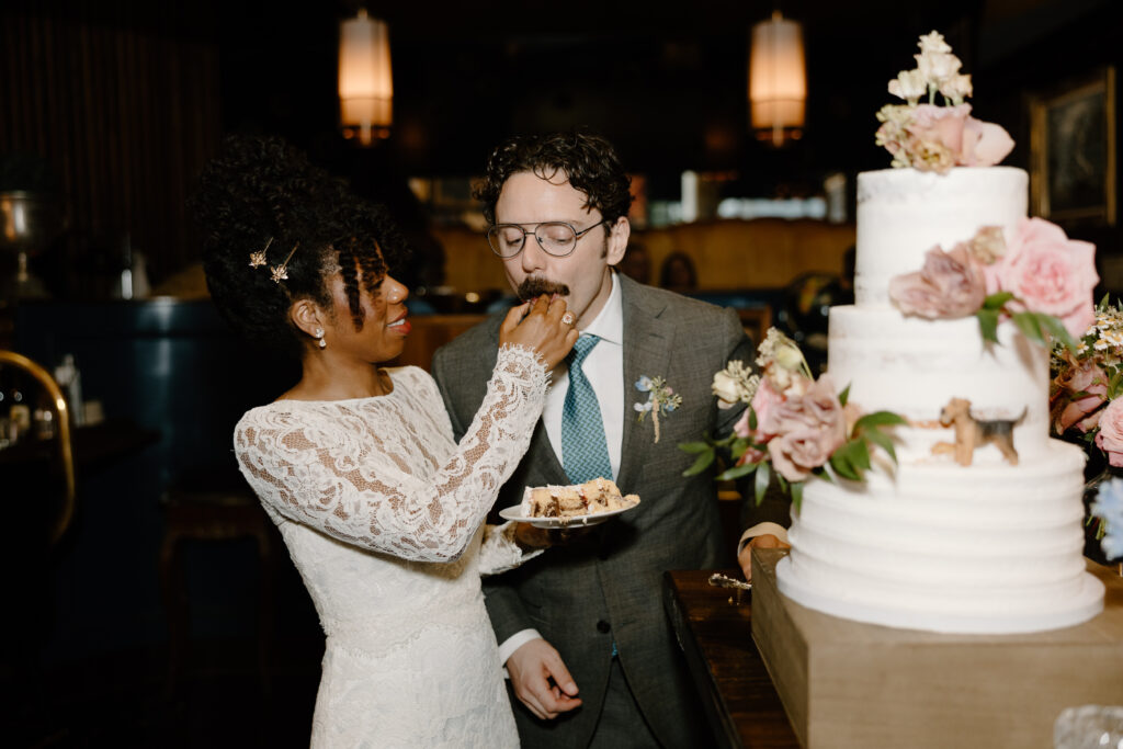 bride serving groom wedding cake with dog topper
